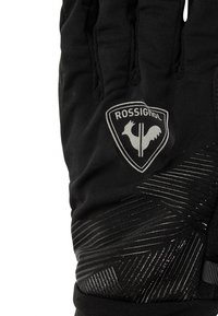 Musta hiihtohanska, jossa on karhennettu pito, hopeinen Rossignol-logo ja erottuva diagonaaliviivojen koristelu sormien ja ranteen alueella.