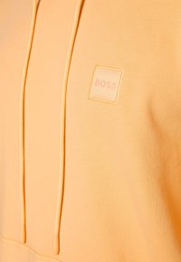 Sweat à capuche en tissu pêche doux avec une finition texturée. Dispose d'une poche avant et d'un petit logo "BOSS" embossé sur la poitrine.