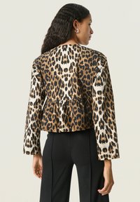 Veste raccourcie en imprimé léopard, avec des teintes noires et dorées, manches longues et bord peplum. Fabriquée en tissu lisse.