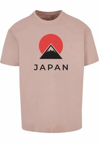 Camiseta de algodón rosa claro con una silueta negra de montaña, un sol rojo arriba y la palabra "JAPÓN" en letras negras en negrita.