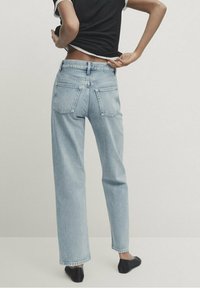 Jeans in denim azzurro chiaro con un design a gamba dritta, cinque tasche e dettagli di cucitura visibili, visti da dietro.