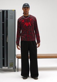 Long-sleeve red jersey with black floral pattern and "AXA" branding, paired with loose-fitting black trousers and black sneakers.