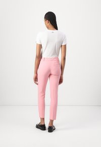 Bílá tričko s krátkým rukávem a růžové tailored kalhoty. Kalhoty mají úzký střih, zadní kapsy a hladkou texturu. Černé boty dotvářejí celkový vzhled.
