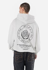 Felpa con cappuccio grigio chiaro e vestibilità oversize. Presenta un grande design grafico nero sul retro, dettagli testuali e polsini larghi.