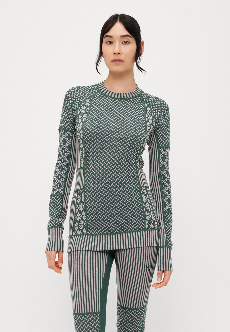 Zöld mintás, hosszú ujjú felső, csíkos részletekkel és testhez simuló fazonnal, amelyhez illeszkedő csíkos leggings tartozik, különböző textúrákkal.