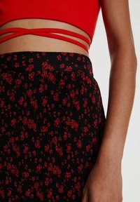 Vue de la taille d'une personne portant un crop top rouge avec des liens à nouer et une jupe plissée noire avec un imprimé floral rouge.