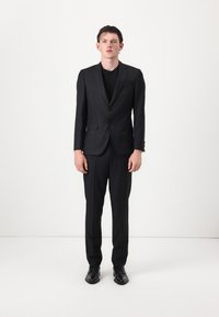 Completo a righe verticali nere con vestibilità slim, giacca monopetto, pantaloni abbinati e scarpe da dress nere, presentato su uno sfondo bianco semplice.