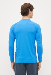 Μπλούζα αθλητική μακρυμάνικη σε �φωτεινό μπλε χρώμα, κατασκευασμένη από απαλό και ελαφρύ υλικό. Διαθέτει ραγλανές μανσέτες και στρογγυλή λαιμόκοψη.