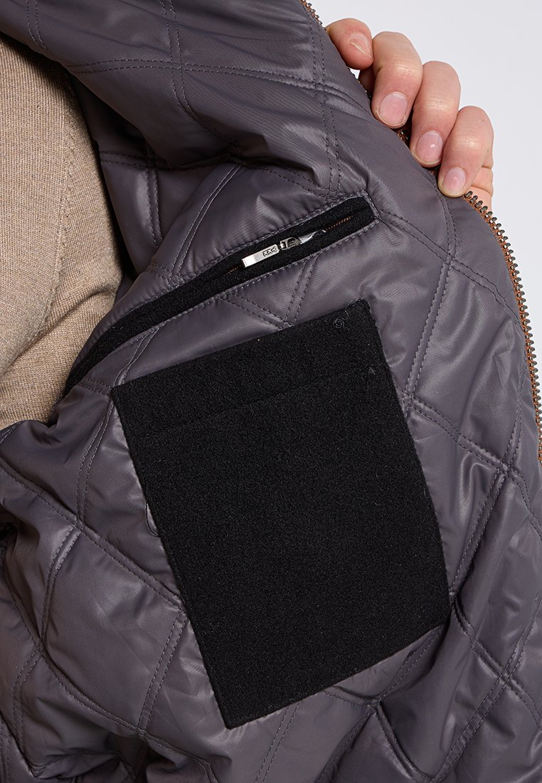 Wnętrze pikowanej szarej kurtki z kieszenią na zamek i rzepem. Gładka faktura z błyszczącym wykończeniem i kontrastowymi detalami z tkaniny.