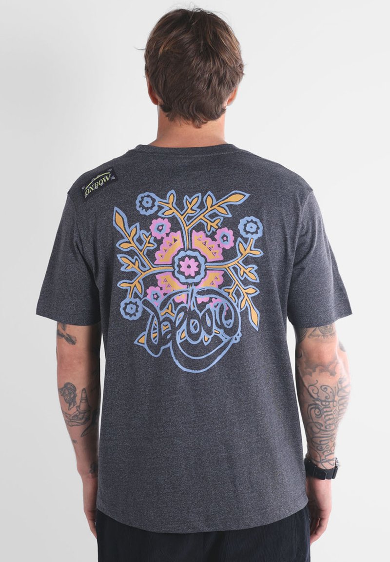 T-shirt gris à manches courtes avec un design floral coloré au dos en rose, bleu et jaune. Comprend une étiquette de marque sur l'épaule.