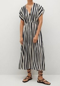 Gestreiftes Maxikleid in Marineblau und Beige, mit tiefem V-Ausschnitt, kurzen Ärmeln, elastischem Bund und fließendem Stoff. Kombiniert mit schwarzen Riemchensandalen.