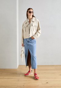 Cropped beige jacket with two front pockets, light blue denim skirt with a front slit, and red and beige sneakers. Simple belt, no visible patterns.