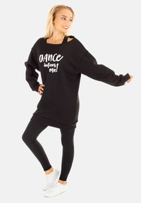 Schwarzes, übergroßes Sweatshirt mit weißem Aufdruck "DANCE defines me!", langen Ärmeln und weitem Ausschnitt, kombiniert mit schwarzen Leggings und weißen Sneakers.
