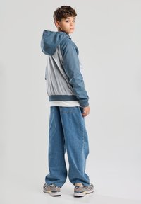 Kevyt huppari, jossa on sininen ja harmaa väri ja rento leikkaus. Yhdistetty löysiin sinisiin farkkuihin ja harmaisiin lenkkikenkiin.