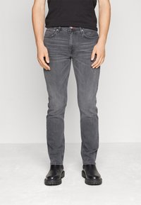 Jeans de mezclilla gris con un corte ajustado, costuras visibles y un ligero efecto de desgaste. Combinados con botas de cuero negras. Diseño minimalista, sin patrones.