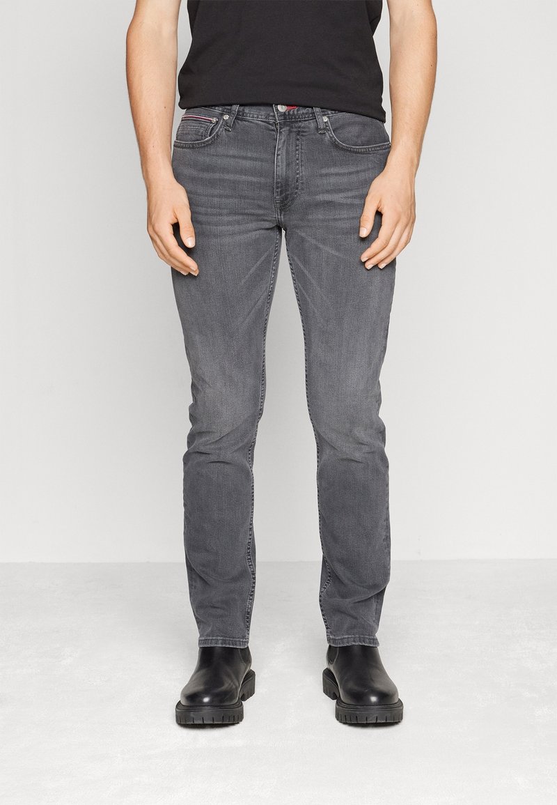 Jeans de mezclilla gris con un corte ajustado, costuras visibles y un ligero efecto de desgaste. Combinados con botas de cuero negras. Diseño minimalista, sin patrones.