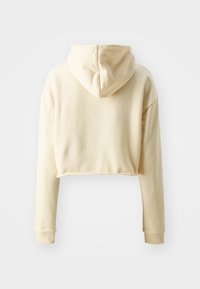 Sweat à capuche court en coton beige doux avec manches longues et capuche ajustable par cordon, doté de poignets côtelés et d'une surface lisse légèrement texturée.