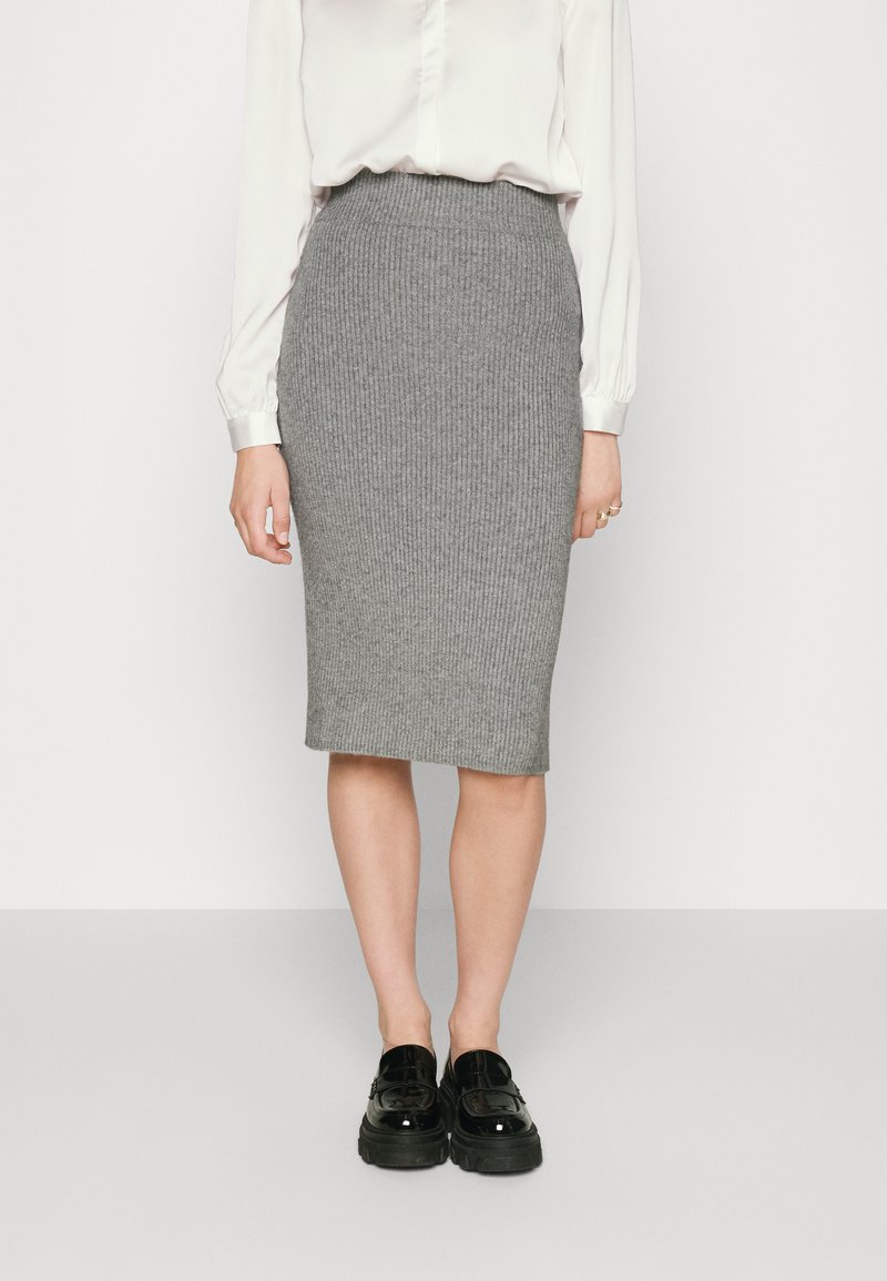 Grijze geribbelde kokerrok met een aangesloten taille en een knielange zoom, gecombineerd met zwarte plateau schoenen en een witte blouse met lange mouwen.