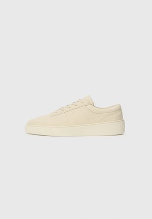 Beige suede lenkkarit, joissa on rakenne pinta, pyöreä kärki, nauhakiinnitys ja paksu kerma-valkoinen kumipohja. Sileä kantapääkoristus.
