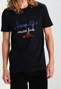 Svart bomullst-shirt med flerfärgad broderad text som läser "lecoqsportif maison fondée en 1882" i blått, vitt och rött.