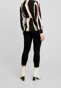 Camicia a righe bianche e nere con vita aderente, abbinata a leggings neri e stivaletti color crema con tacco a blocco. Tessuto di texture liscia.