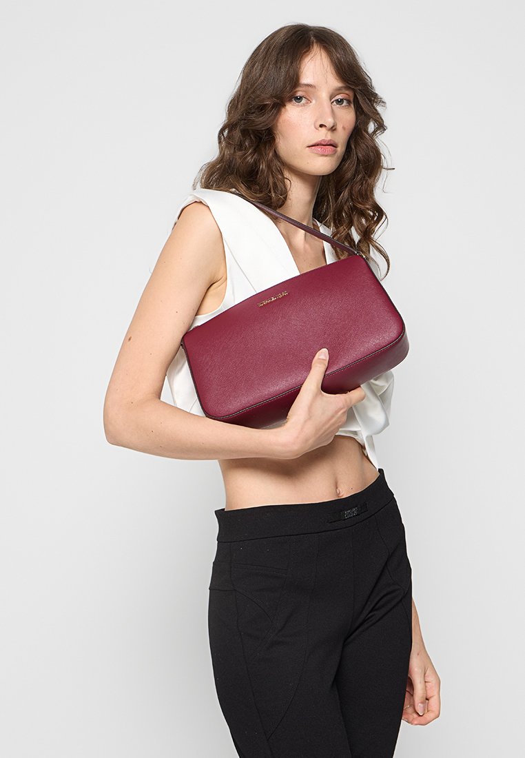 Borsa a mano in pelle bordeaux con un design strutturato, manico corto e marchio dorato discreto. Texture liscia, forma rettangolare e senza motivi visibili.