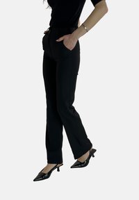 Sorte skræddersyede bukser med forlommer, slank pasform, glat tekstur og subtile syningsdetaljer, kombineret med spidse sorte hæle.