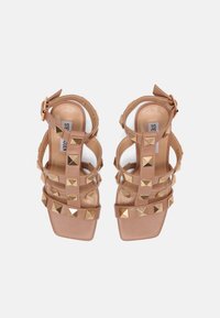 Sandales nues à brides avec bouts carrés et clous pyramides dorés, fermetures à boucle à la cheville et semelles rembourrées.