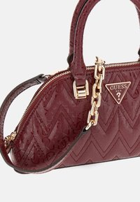 Bordeaux patentlæder Guess håndtaske med quiltet chevron mønster, guldkæde-detalje, doble håndtag og fronttriangulært logo badge.