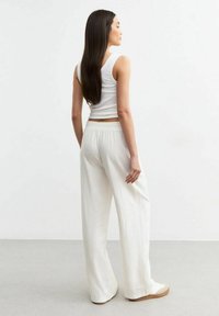 Pantalones anchos blancos hechos de una tela ligera, con una cinturilla elástica y una textura suave, combinados con una camiseta sin mangas blanca ajustada.