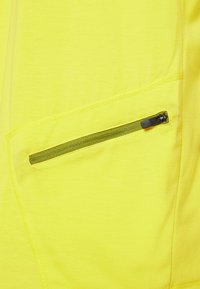 Haut en tissu jaune avec une poche zippée dotée d'une fermeture éclair verte foncée et des coutures le long des coutures. La texture semble lisse.