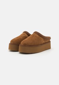 Brown suede slip-on clogs with a rounded toe, featuring a thick brown platform sole and padded collar for comfort.