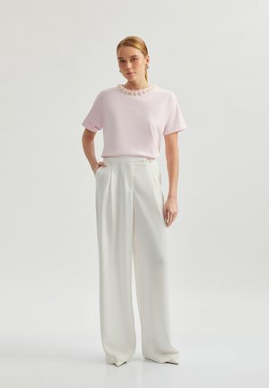 Chemise rose à manches courtes avec un col floral texturé, associée à un pantalon large taille haute blanc. Tissu lisse, coupe élégante.