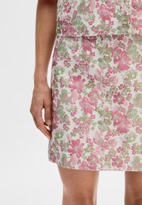 Jupe à motifs floraux présentant des fleurs roses et vertes sur un fond blanc, fabriquée en tissu léger avec une coupe droite et une couture invisible.