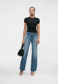 Czarna dopasowana koszulka, jasnoniebieskie dżinsy z wysokim stanem w kształcie dzwonów, białe sandały oraz czarna torebka o teksturowanej powierzchni. Prosty, codzienny wygląd, gładki materiał.