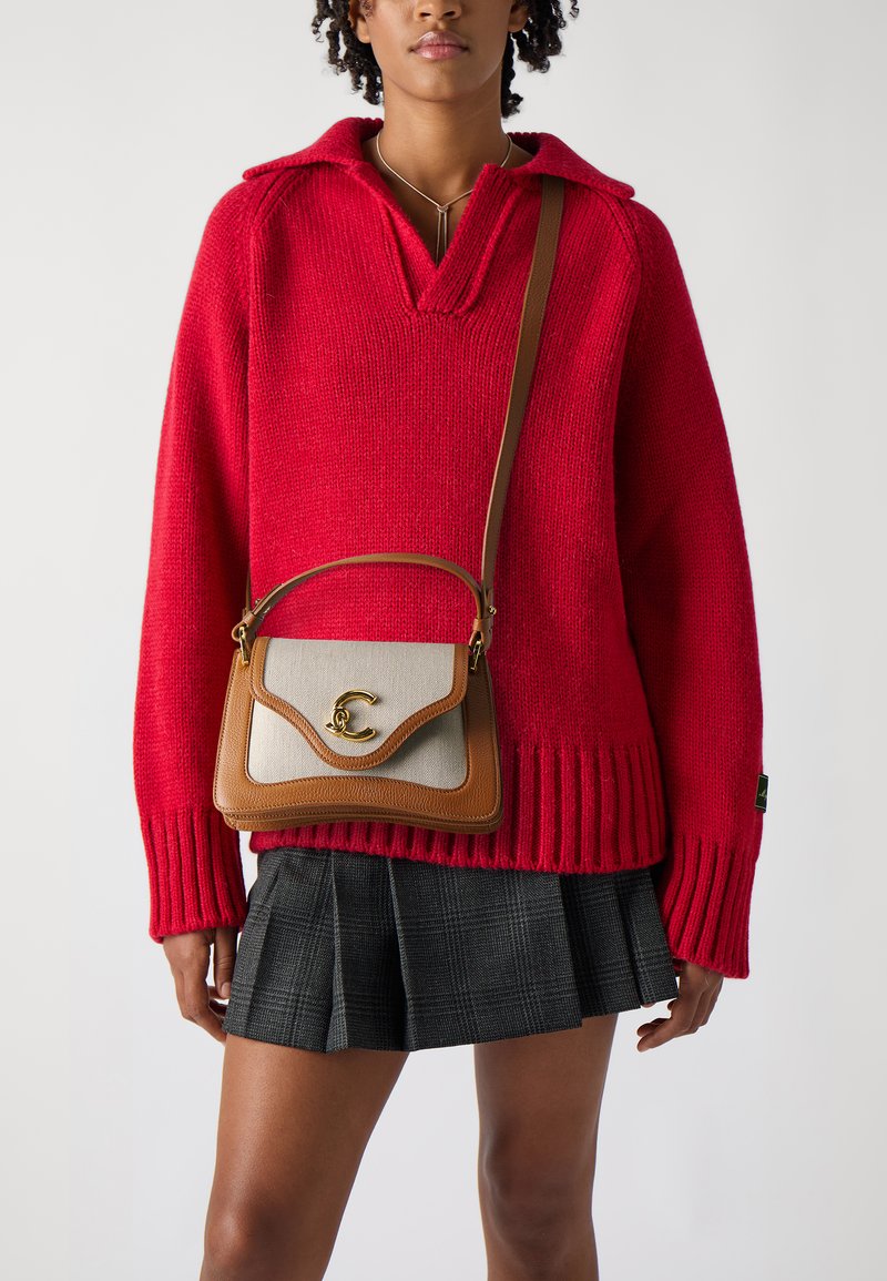 Maglione rosso lavorato a maglia con colletto, abbinato a una borsa a tracolla marrone e beige con un accento dorato. Gonna a quadri con pieghe.
