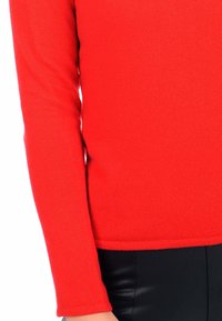 Rotes Strickoberteil mit langen Ärmeln, rundem Halsausschnitt, leicht strukturiertem Stoff und geradem Saum. Kombiniert mit schwarzen, figurbetonten Leggings.