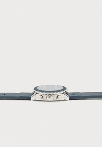 Reloj cronógrafo con una correa de silicona azul oscura, caja de acero inoxidable plateado y una esfera negra texturizada que presenta detalles plateados y botones de presión.