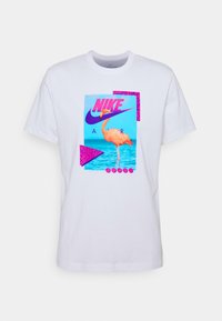 Vit bomulls t-shirt med en färgglad grafisk design som visar en flamingo, blått vatten och texten "NIKE AIR" i rosa och lila.