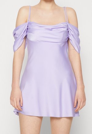 Mouwloze lavendelkleurige minijurk met gedrapeerde off-shoulder mouwen en dunne dubbele spaghettibandjes bij een staande persoon.