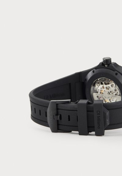 Black rubber watch with a textured strap, featuring a round case, metal accents, and a visible movement through the back.