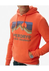 Sudadera naranja con un gráfico de montaña y un diseño de atardecer. Cuenta con un bolsillo frontal tipo canguro y cordones ajustables. Corte regular y tejido texturizado.