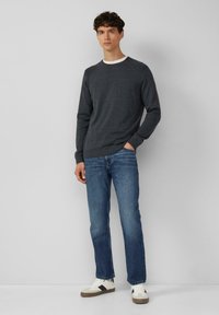 Ciemnoszara sweter z dzianiny z okrągłym dekoltem, połączony z niebieskimi spodniami typu straight-leg i białymi sneakersami z brązowymi i czarnymi akcentami.
