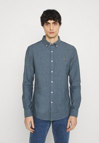Overhemd met knoopsluiting in donkerblauwe stof, met een kraag, lange mouwen en witte knopen. Klein geborduurd logo op de borst.