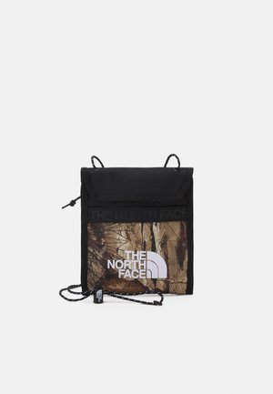 Kleine zwarte en bruine schoudertas met The North Face-logo en verstelbare koordband op een effen witte achtergrond.