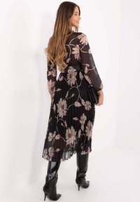 Schwarzes plissiertes Kleid mit Blumenmuster in Rosatönen, langen Ärmeln, tailliert, kombiniert mit schwarzen Stiefeln mit hohem Absatz und Clutch.