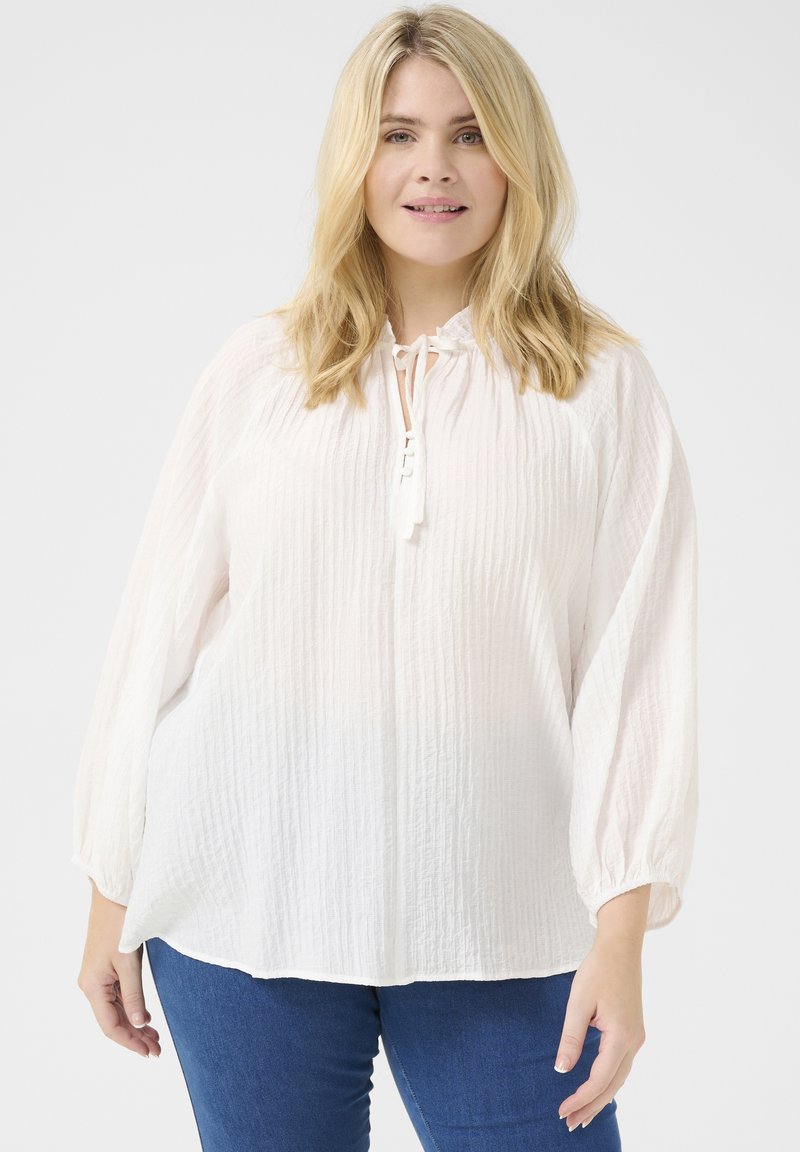 Lightweight, semi-sheer white blouse with textured fabric, gathered balloon sleeves, and a neck tie. Paired with blue denim jeans.