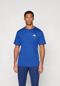 Blue short-sleeved athletic shirt with a round neck and a white logo accent on the left chest. Fabric appears lightweight and textured.