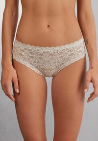 Lace hipster slips in lichtbeige. Kenmerken zijn bloem- en geometrische patronen, golvende randen en een zachte, delicate textuur van de stof.