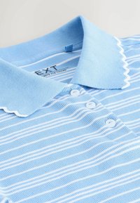 Polo azzurro chiaro con righe orizzontali bianche, colletto smerlato e chiusura con tre bottoni. Realizzata in una miscela di cotone strutturato.